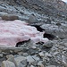 Stark unterhöhlte Reste des Galengletschers im Talboden, im Kontrast zu den Schneealgen im Schnee.