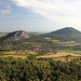 Gipfel Kaňkov - Teilpanorama 6/7. Ausblick in etwa südliche Richtung u. a. auf die markanten Bergkegel von Zlatník (rechts) und Želenický vrch (links) sowie auf den Ort Želenice (vorn).