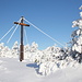 Pramenáč - Ein kleines Stück abseits des heute verschneiten Waldwegs steht ein großes Gipfelkreuz.